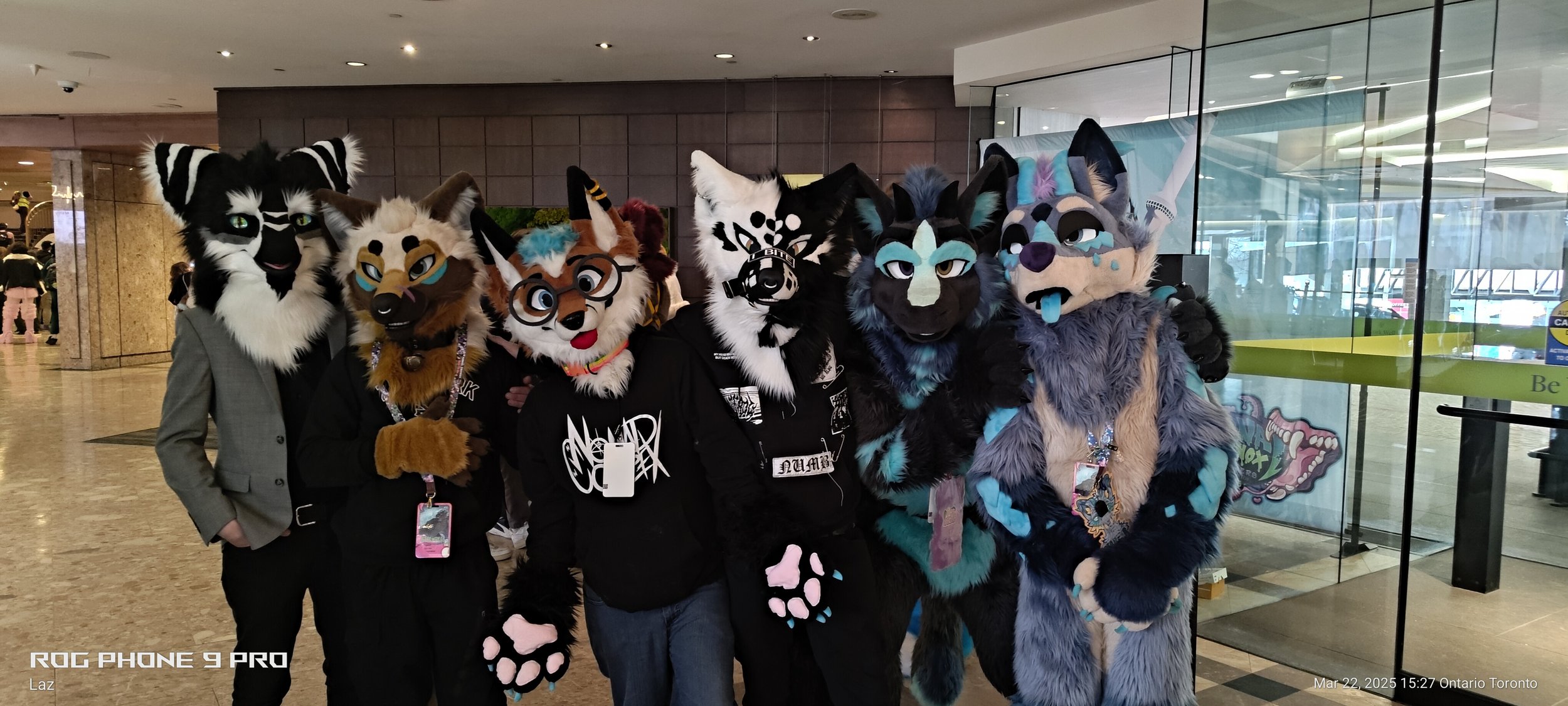 A group of people in colorful animal costumes or fursuits posing together in an indoor setting.