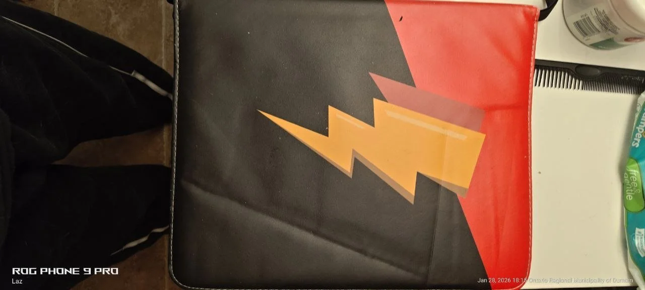 A binder with a lightning bolt symbol on a red and black background, placed on a desk with other items.