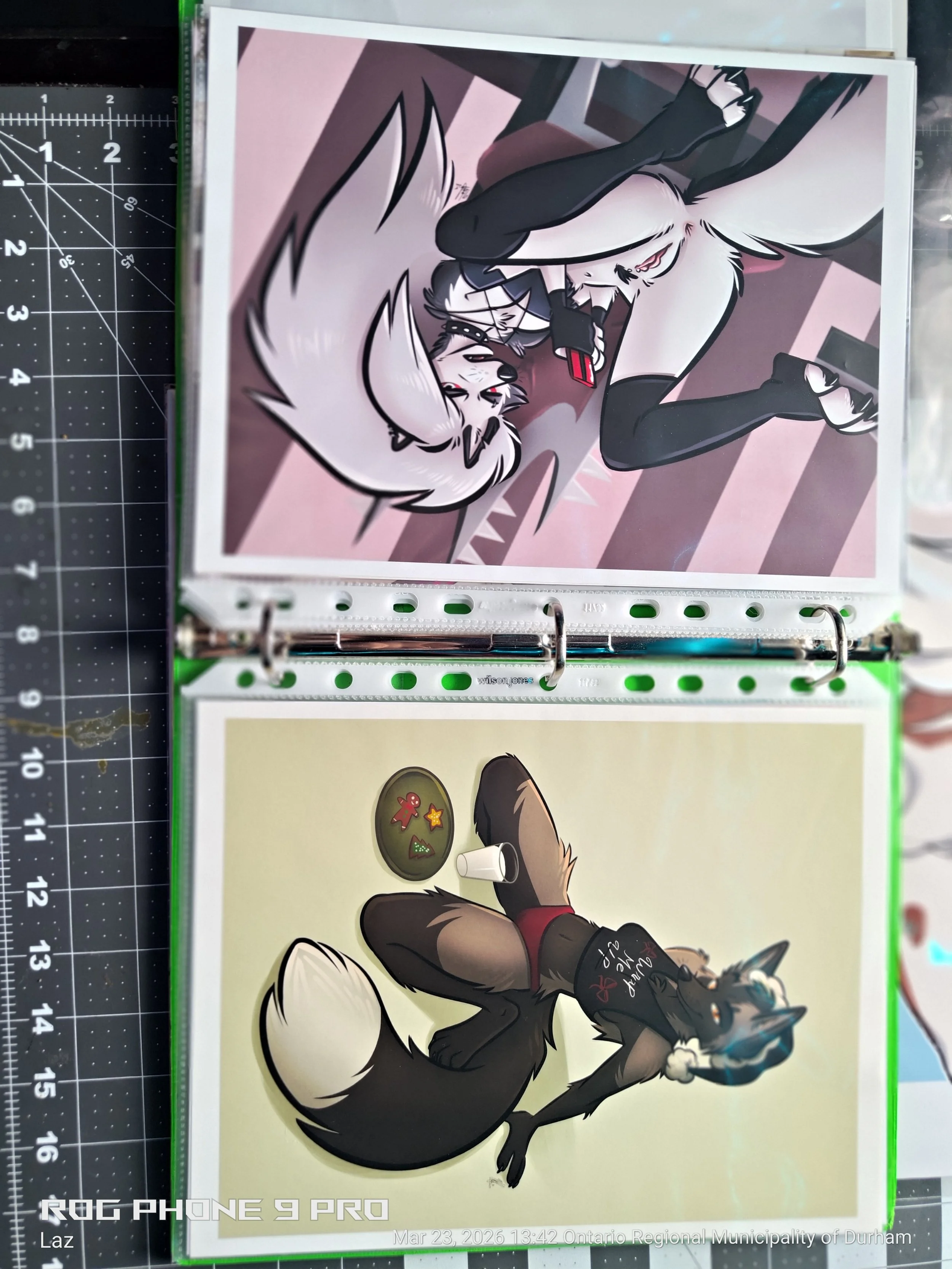 A digital illustration featuring anthropomorphic wolf characters. One wolf, lying on its back, wearing a black shirt with a red design and fangs showing, is in a playful pose. The other wolf, with white and black fur, is resting its head on a pink pi
