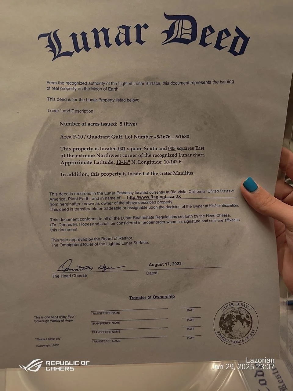 A document titled 'Lunar Deed' certifying the ownership of 5 acres of lunar land, signed and dated August 17, 2022, with official stamps and signatures, held by a person with painted blue nails.