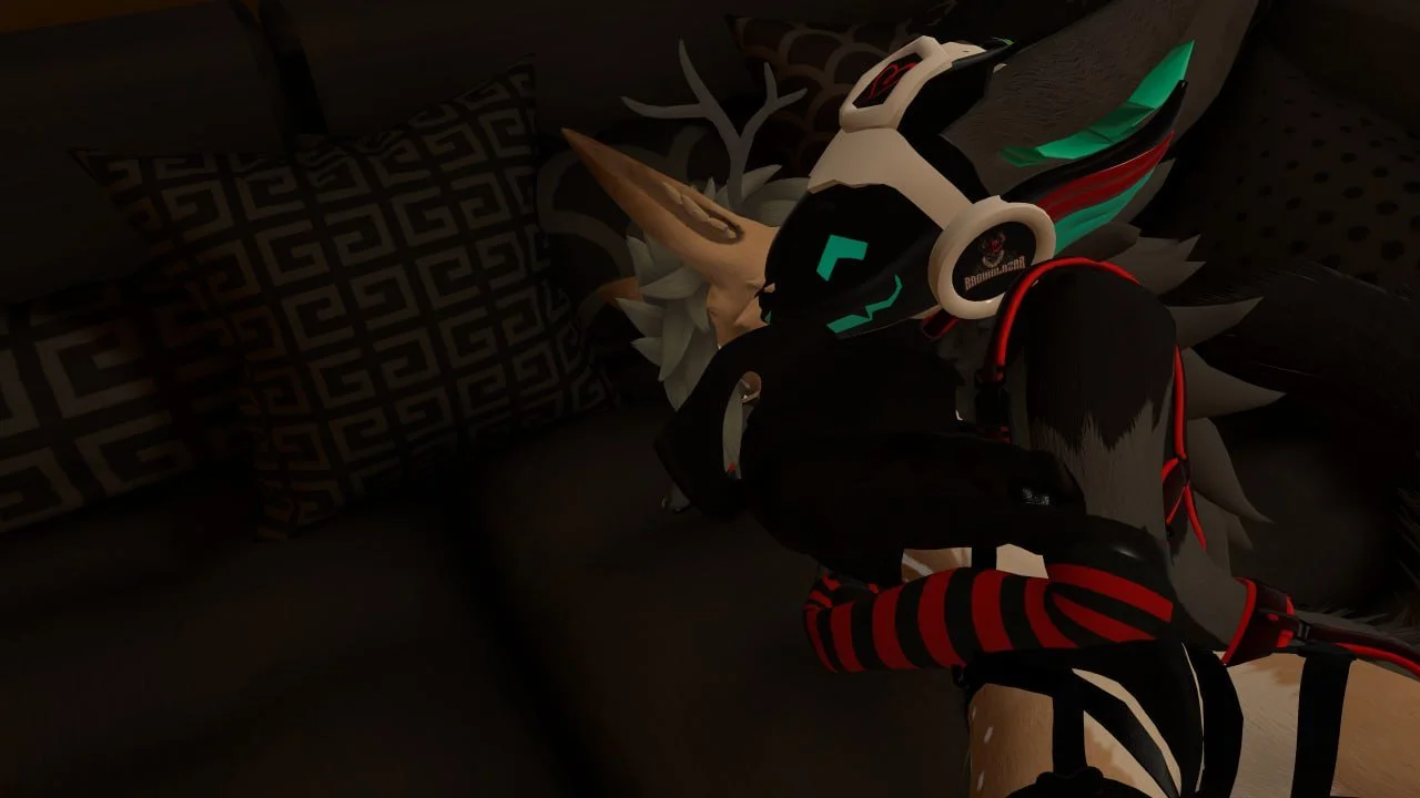 A computer-generated character with a dark face, glowing blue eyes and markings, wearing headphones with a gaming logo, in front of a decorative pillow and a plush deer head on a black sofa.