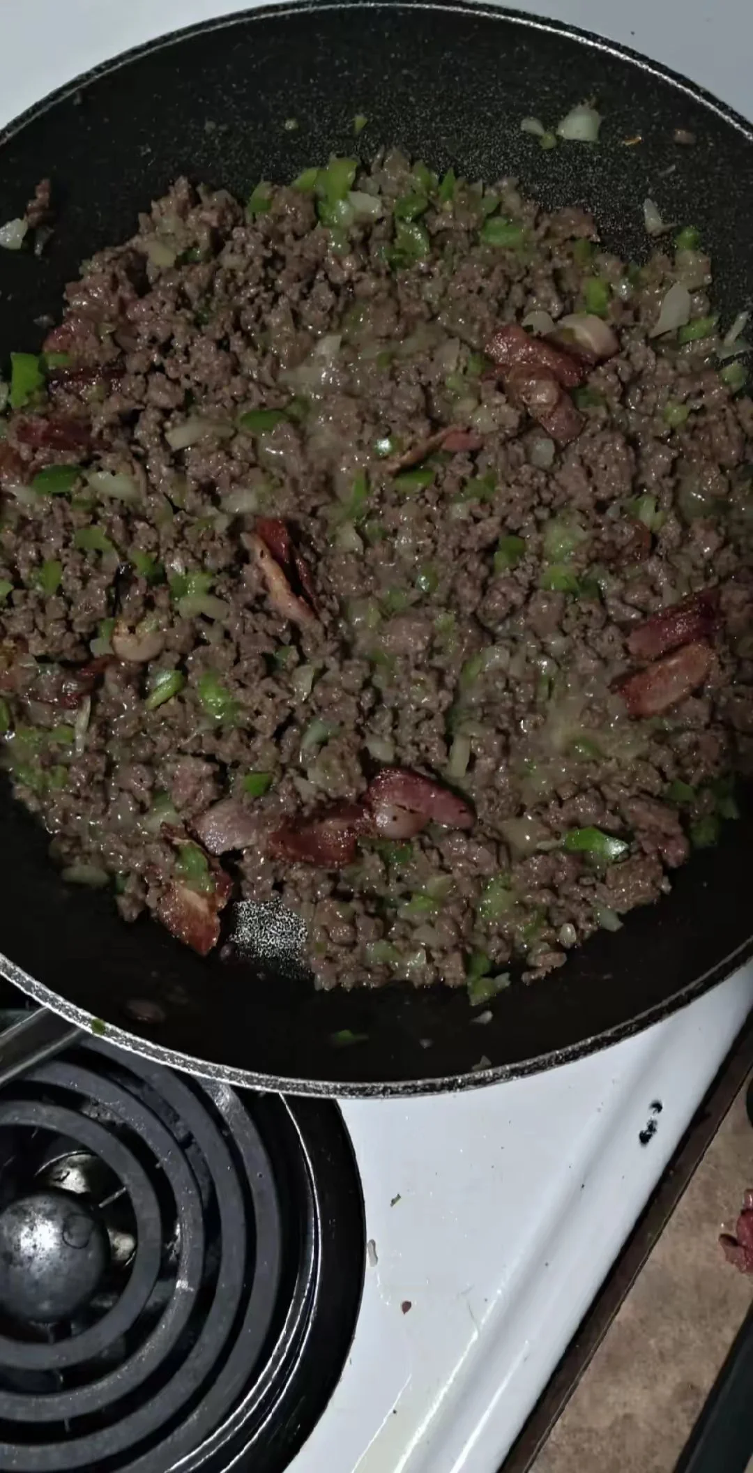 Ground beef being cooked with chopped onions and green bell peppers in a skillet on a stovetop.