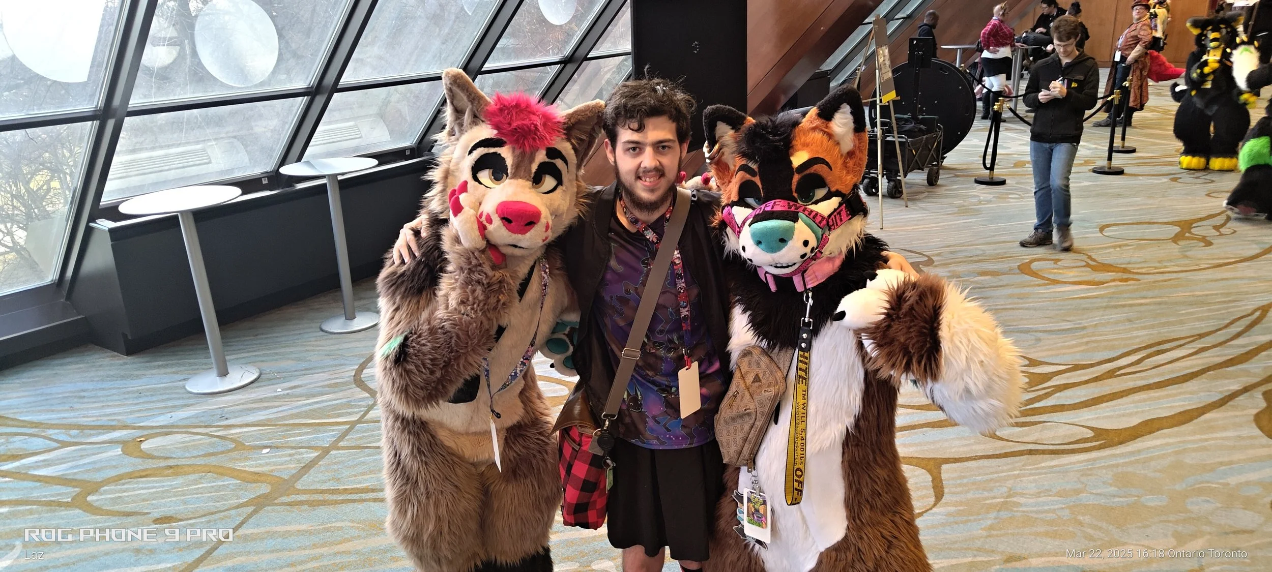 Person posing with two individuals dressed in colorful furry animal costumes in a large indoor convention center.