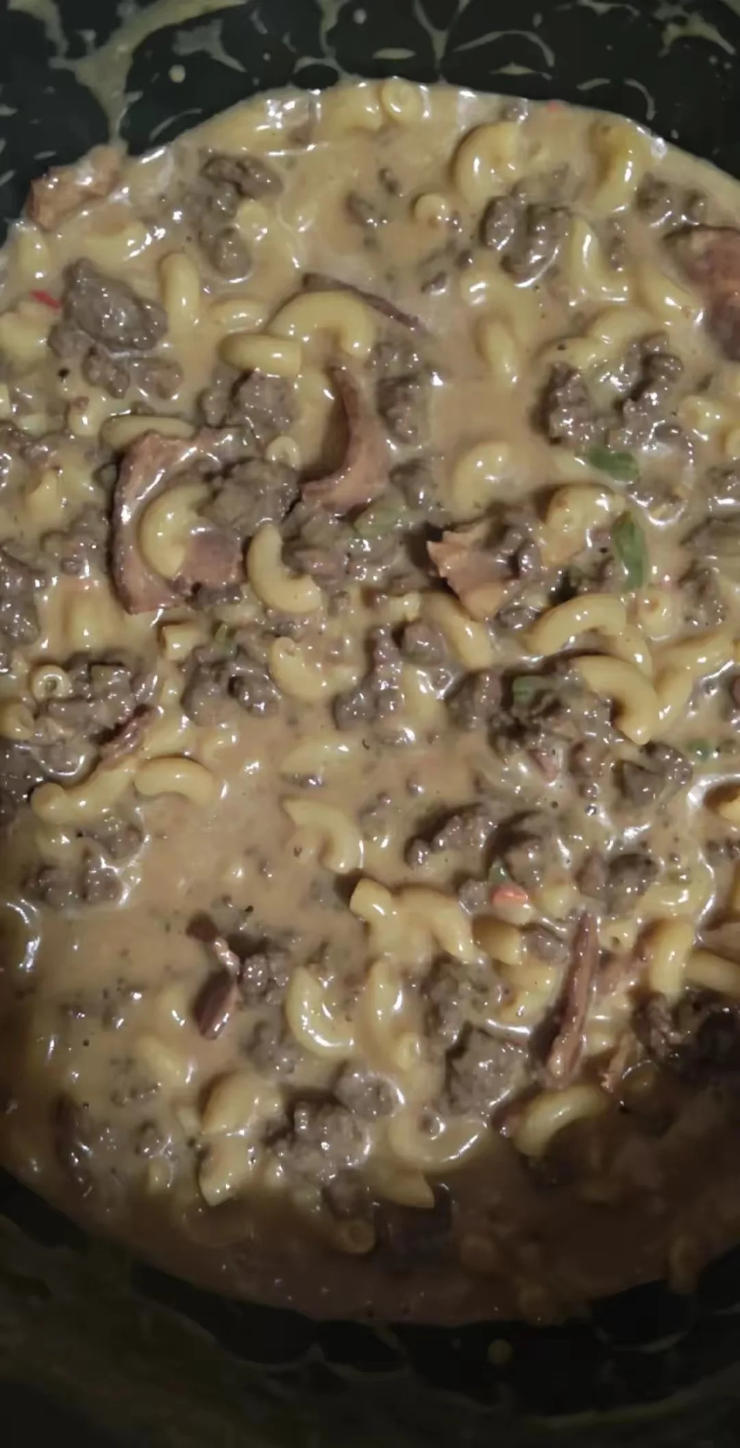 Cooked macaroni and beef with creamy sauce in a black skillet.