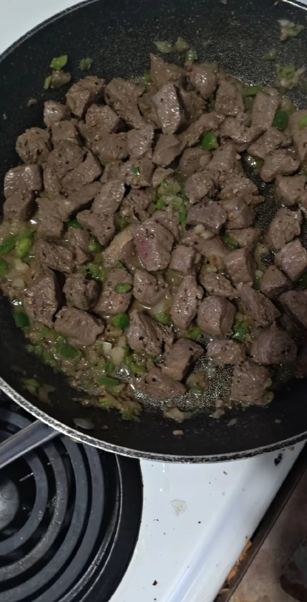 Cooked chopped beef with green onions in a frying pan on a stovetop.
