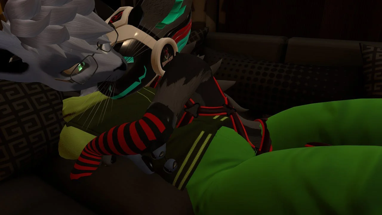 A person wearing a wolf mask with glasses is lying on a couch, holding a video game controller, with a dark background and patterned pillows around.