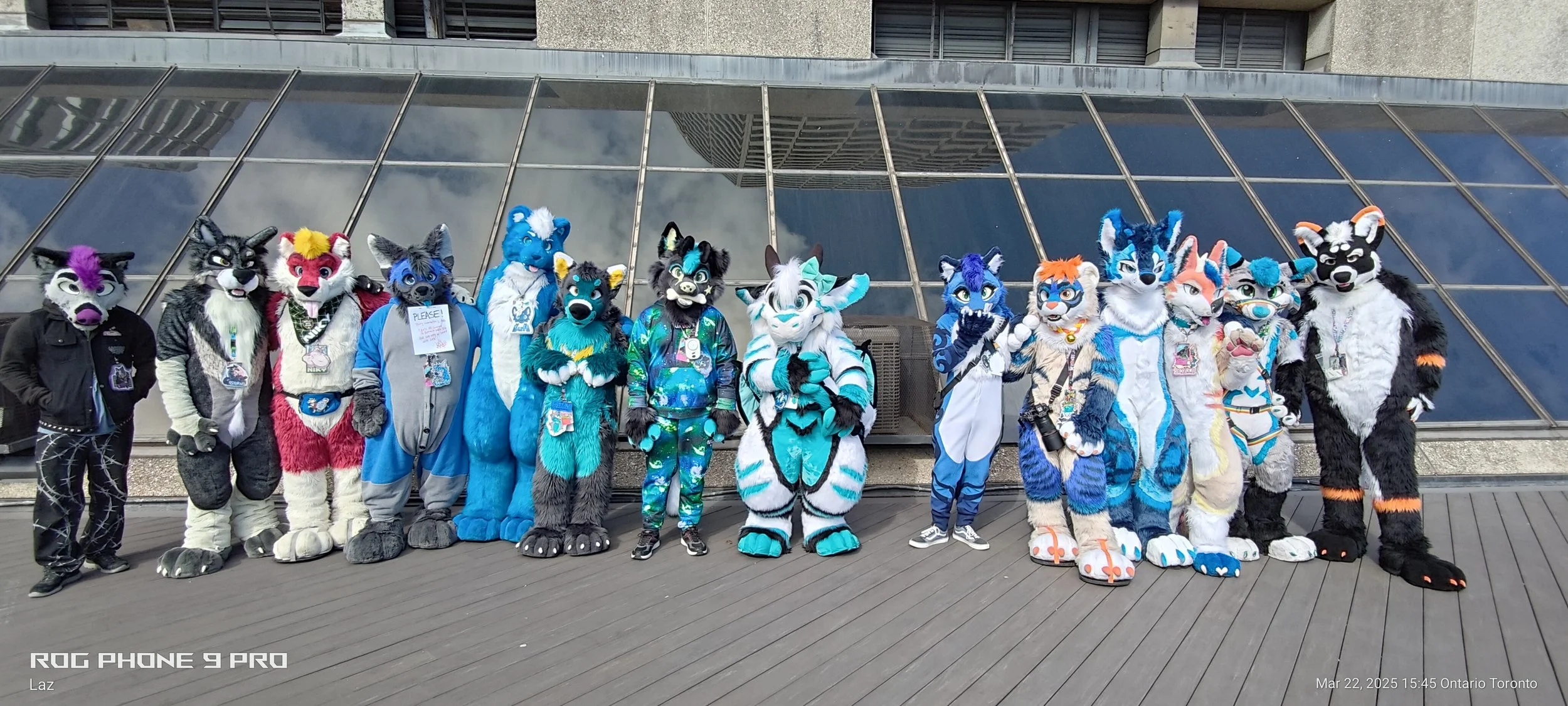 A group of individuals dressed in colorful furry animal costumes, known as fursuits, standing in front of a modern building with glass panels.
