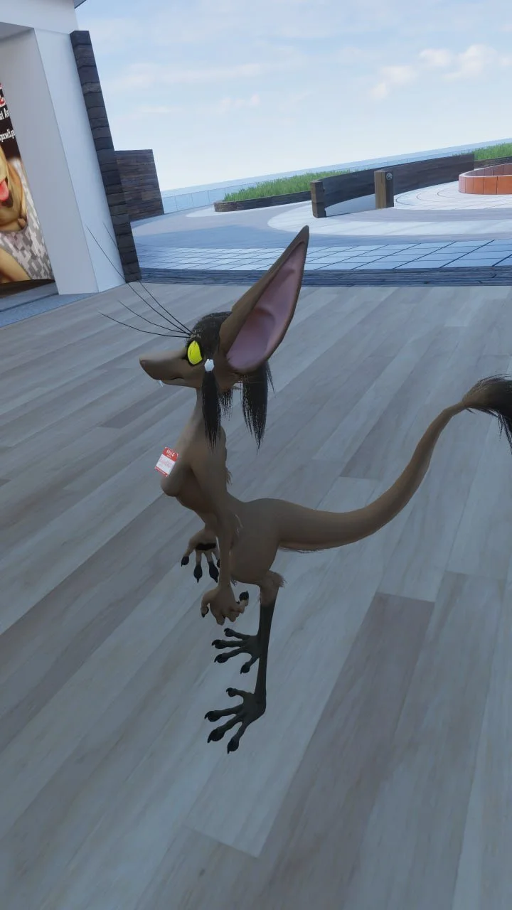 A cartoonish pterosaur figure with large ears, yellow headphones, and a tag around its neck, standing on a wooden floor in a modern outdoor area.