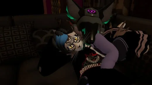 A person in a purple hoodie lying on a couch with an anthropomorphic wolf mask, next to a gray tabby cat with blue hair, in a dimly lit room.