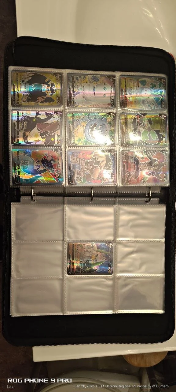 A black binder with nine Pokémon trading cards in plastic sleeves on the top row and one card on the bottom row. The cards feature holographic images of various Pokémon.