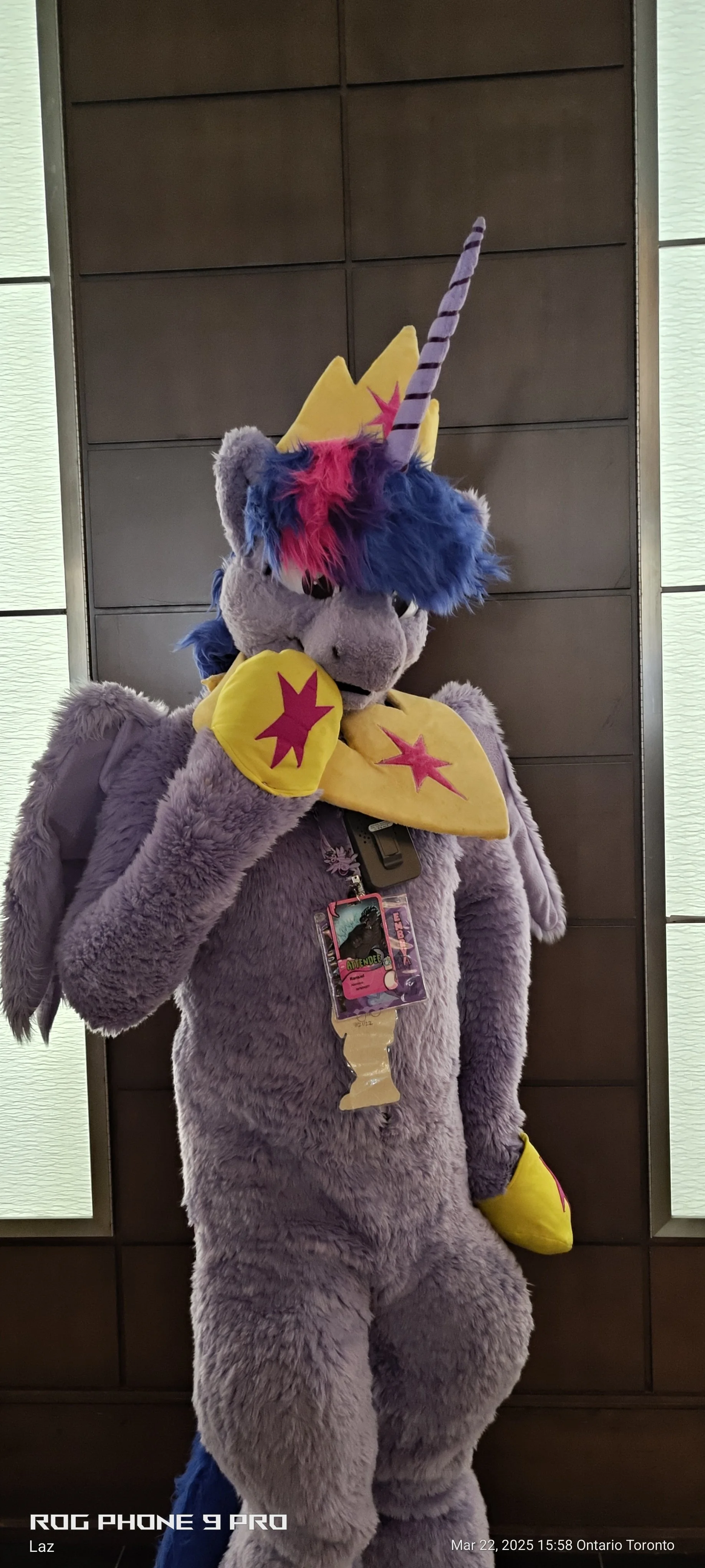 A person dressed in a purple unicorn costume with a mane, horn, wings, and star decorations, standing in front of a wooden wall, at an event in Ontario Toronto.