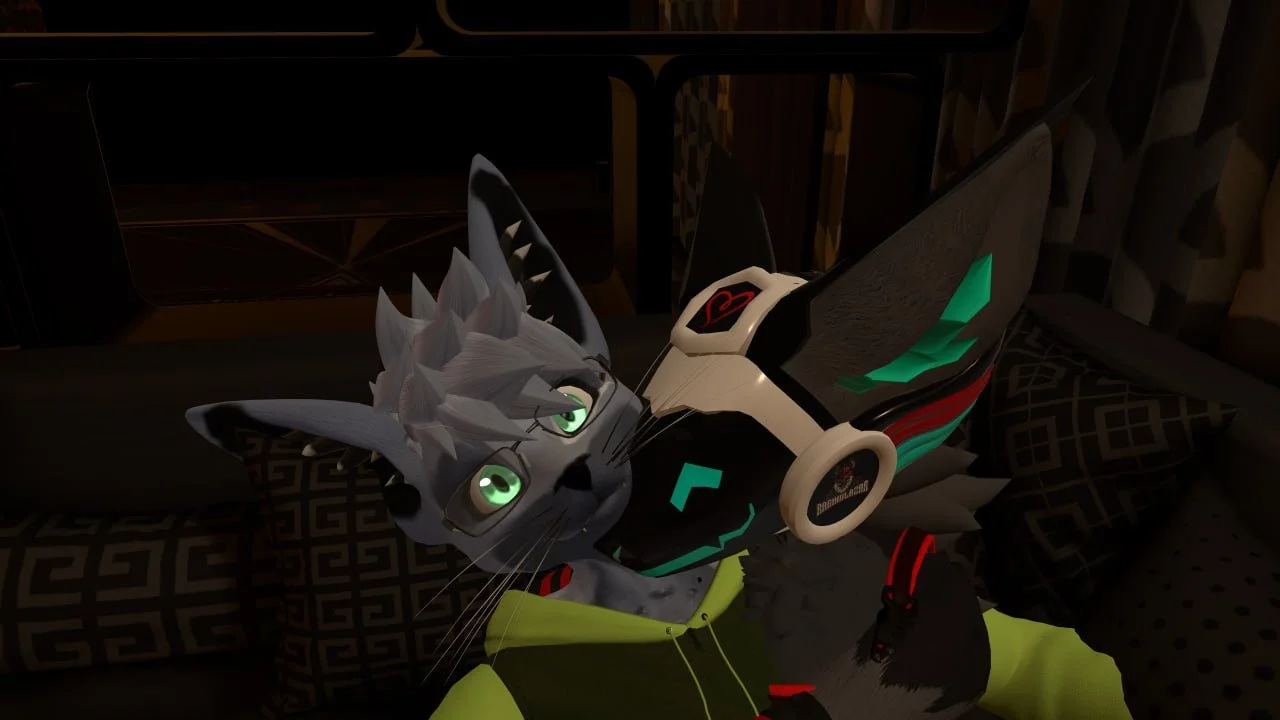 An animated anthropomorphic cat character with green eyes, gray fur, and horns, lying on a bed in a room with patterned pillows, wearing a high-tech suit and headphones.