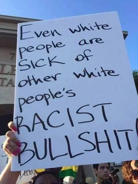 Person holding a sign that reads, "Even white people are sick of other white people's racist bullshit."