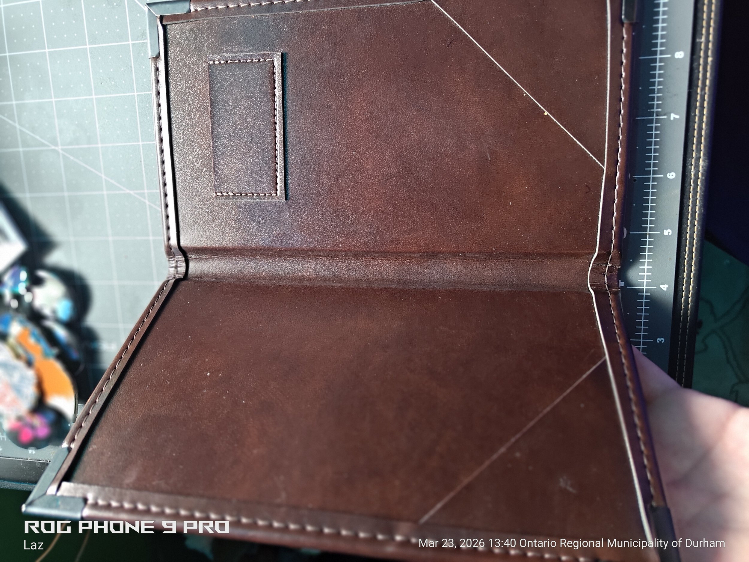 A brown leather-bound journal or notebook with a stitching design along the edges, partially opened on a cutting mat.