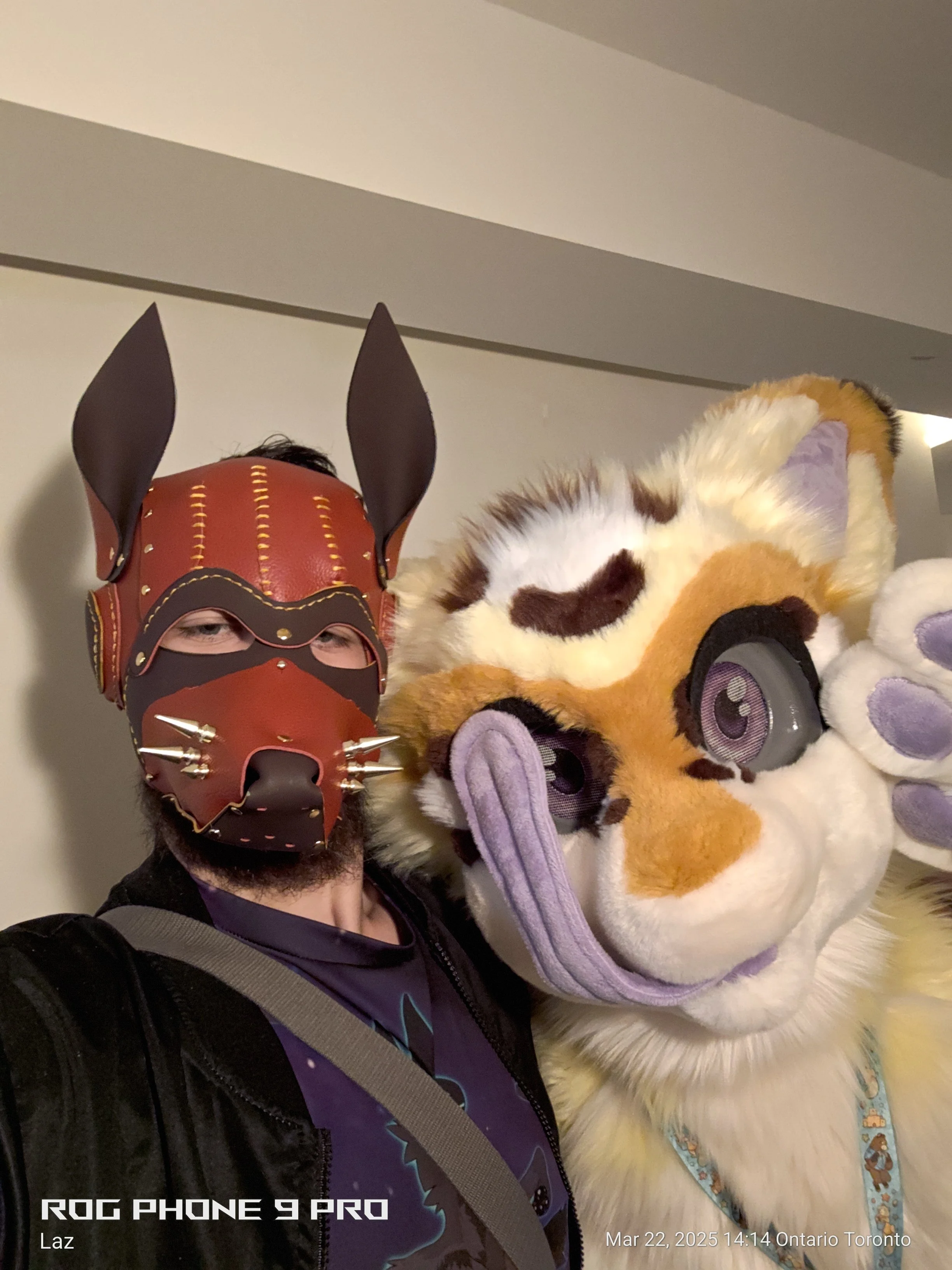 Person wearing a red and black animal mask with tall ears next to a large plush lion costume with purple accents and big eyes.