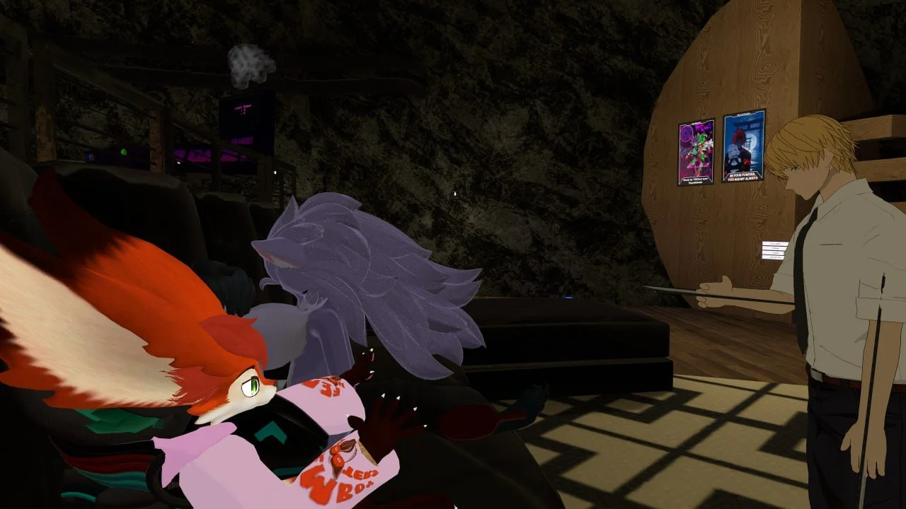 A digital artwork featuring anthropomorphic characters in a dimly lit room. One character is a fox with orange and white fur, wearing a shirt with the words "Lick Bomb" on it, and the other is a gray, wolf-like figure with long hair. A human (or huma