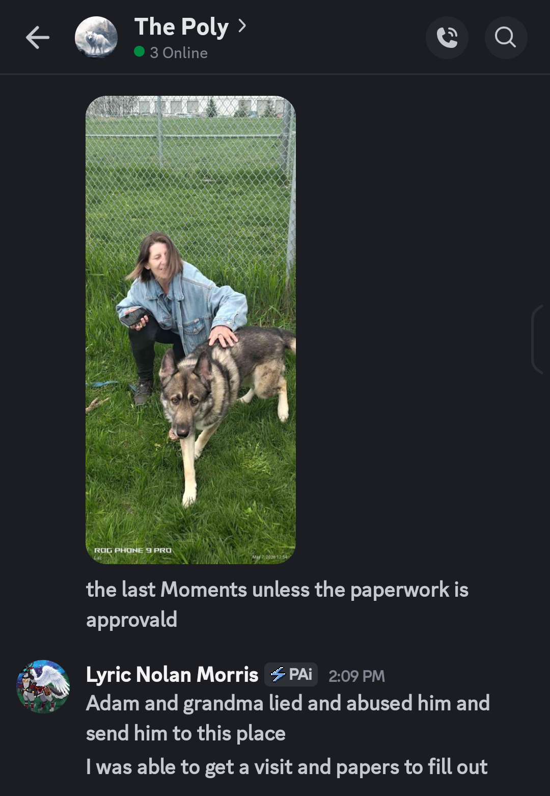 A woman kneeling on grass with a large Siberian Husky dog in front of her, near a chain-link fence, on a cloudy day.