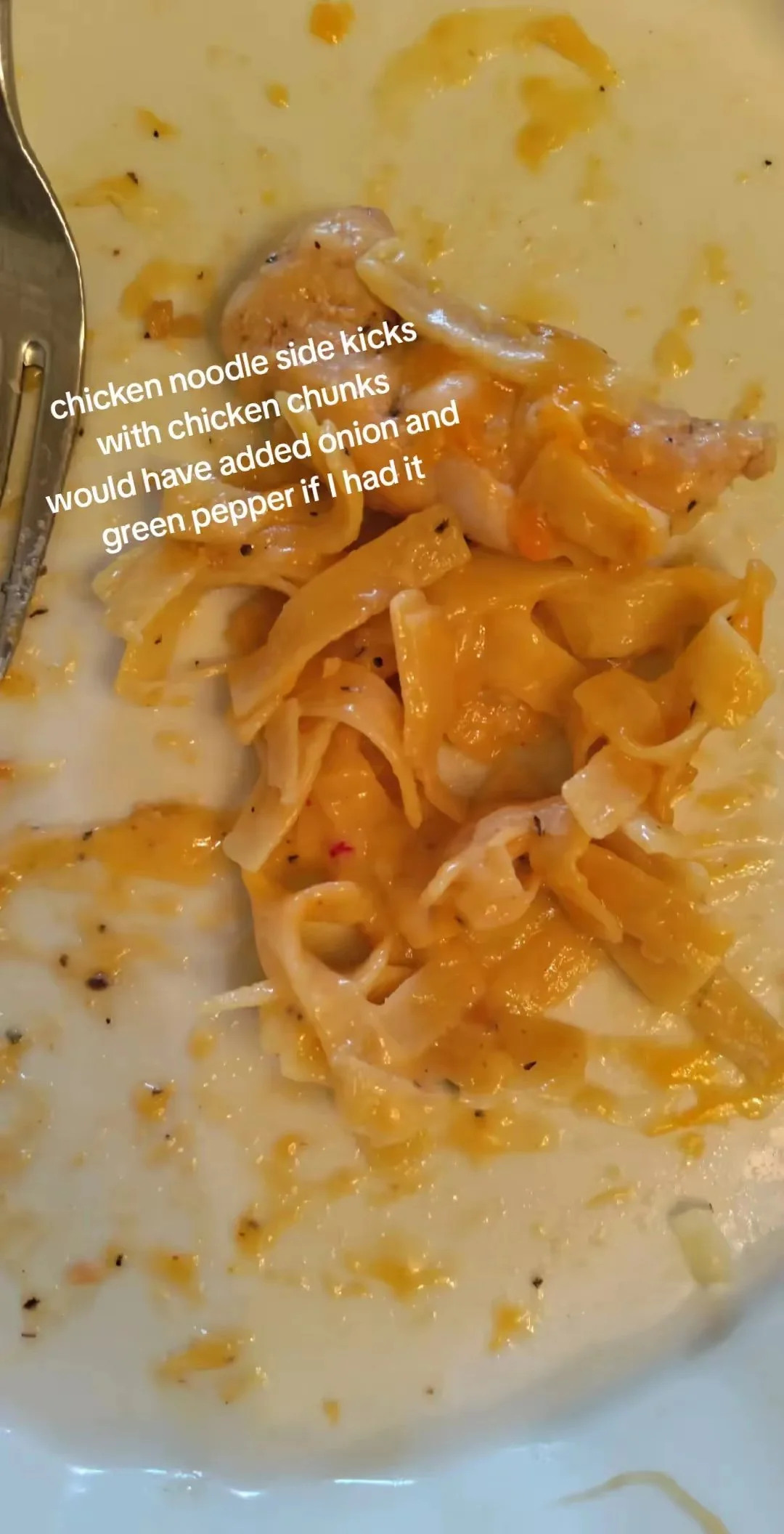 Partially eaten bowl of chicken noodle soup with chicken chunks, onion, and green pepper, with some broth visible and black pepper.