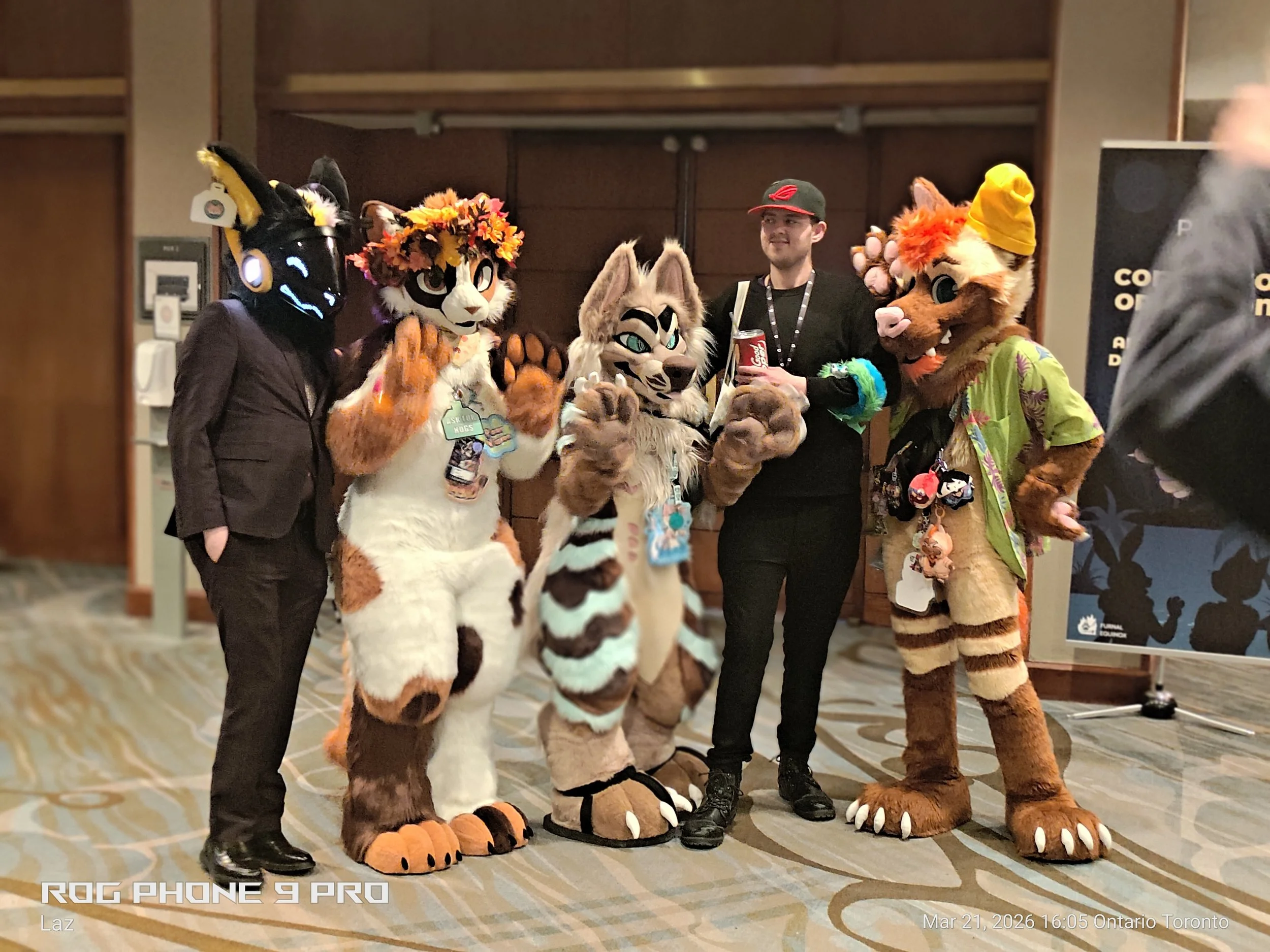 Group of people dressed in colorful animal costumes standing with a person wearing a black shirt and hat in an indoor setting.