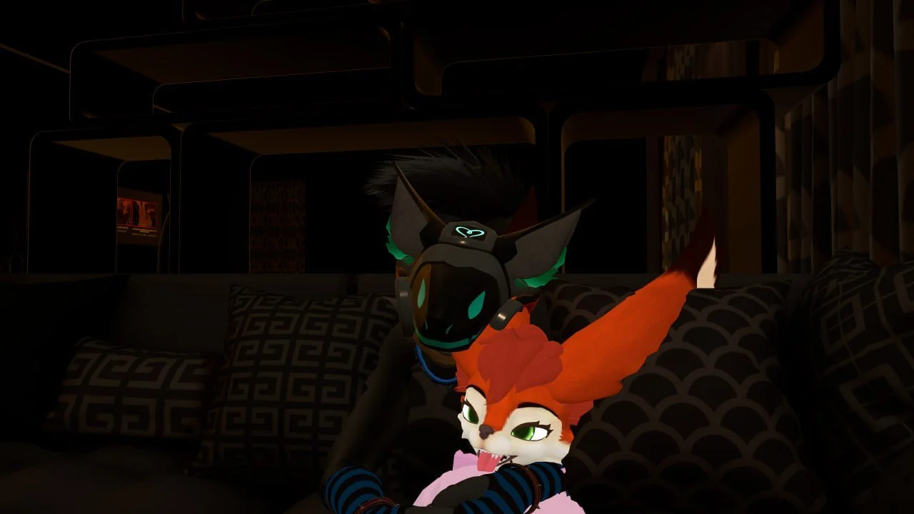 Two anthropomorphic fox characters, one with orange fur and the other with black, inside a dimly lit room. The black fox is wearing a headset with a glowing green symbol, while the orange fox is leaning on a sofa with patterned pillows.