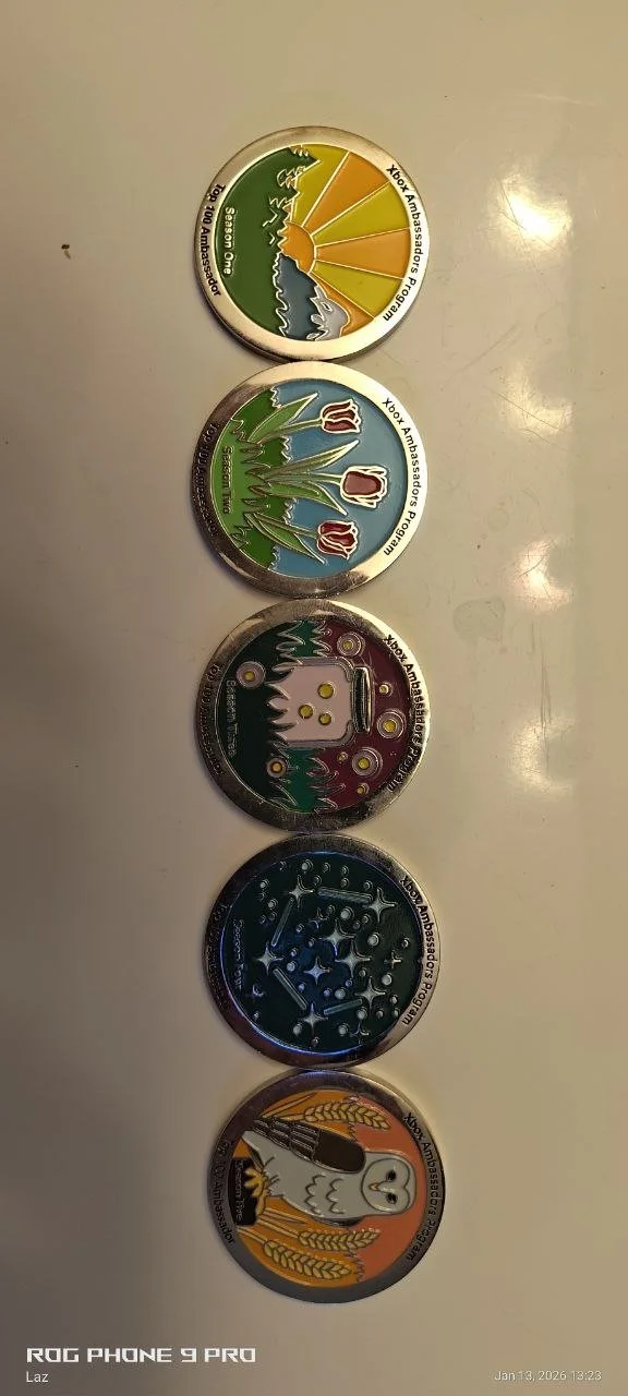 A vertical arrangement of five Nintendo Xbox Ambassador coins featuring various designs, including a sunset scene, a row of red mushrooms, a ghostly face, a constellation map, and a bird with wheat, on a white surface.