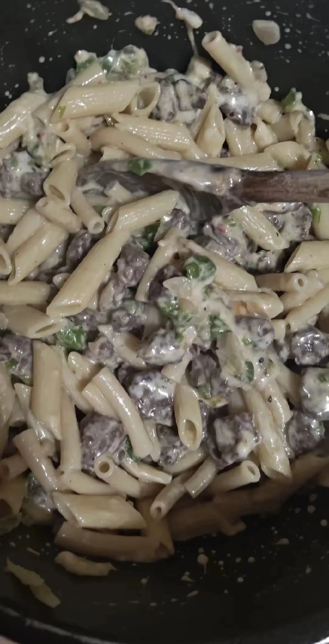 Creamy pasta with penne, mushrooms, and chopped green herbs in a skillet.