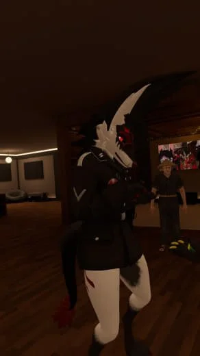 Person in a black and white costume with a mask, standing indoors, with another person in the background.