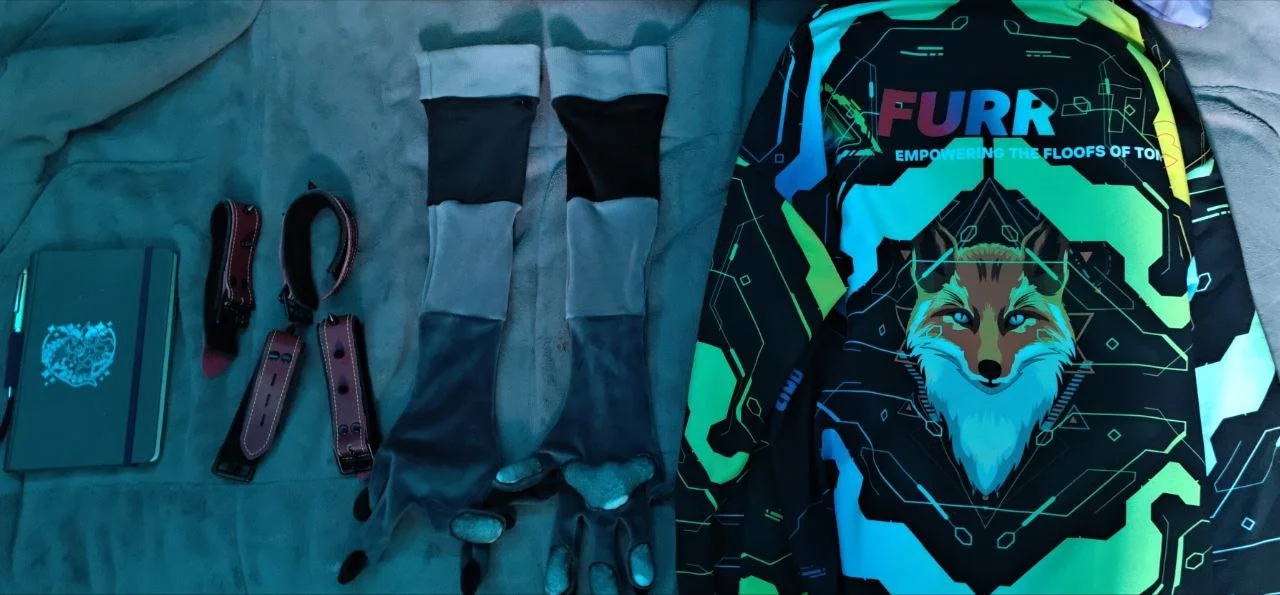 Collection of gear for a dog, including two leashes, a pair of gloves, a closed notebook, and a colorful jacket featuring a fox graphic and the words "FURR" and "EMPOWERING THE FLOORS OF TOP".