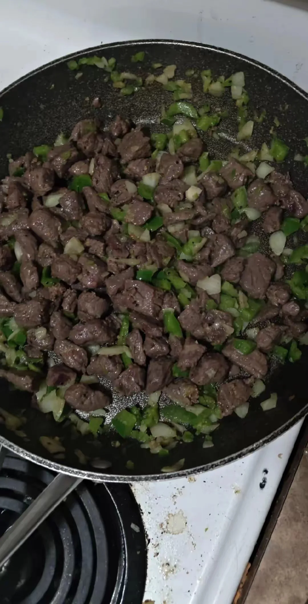 Sautéed beef and chopped green onions in a black frying pan on a stove.