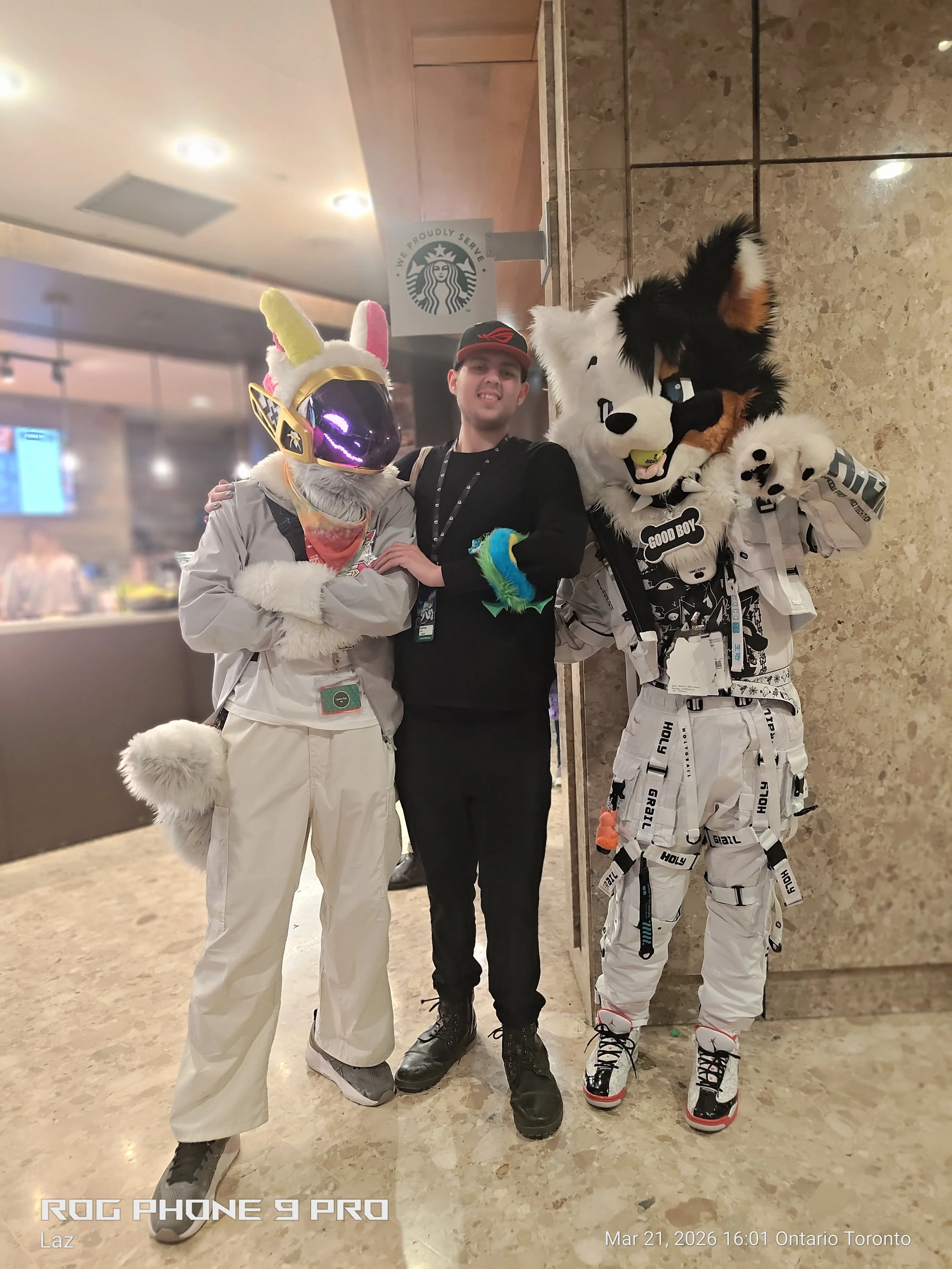 A person with Sonic the Hedgehog costume and two people in costumes with animal heads, standing inside a building near a wall with a Starbucks sign.