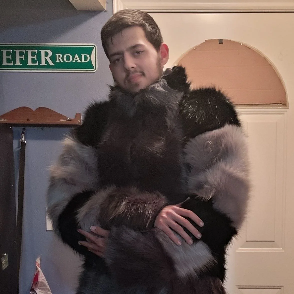 A young man holding a large, fluffy dog in an indoor setting with a blue wall, a sign that reads 'EFFER ROAD', and a door in the background.