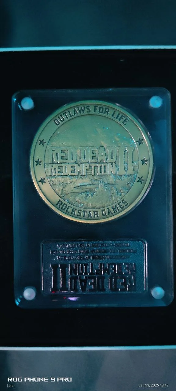 Gold coin featuring the game logo for Red Dead Redemption 2, with phrases 'Outlaws for Life' and 'Rockstar Games' and imagery of a landscape and two figures.