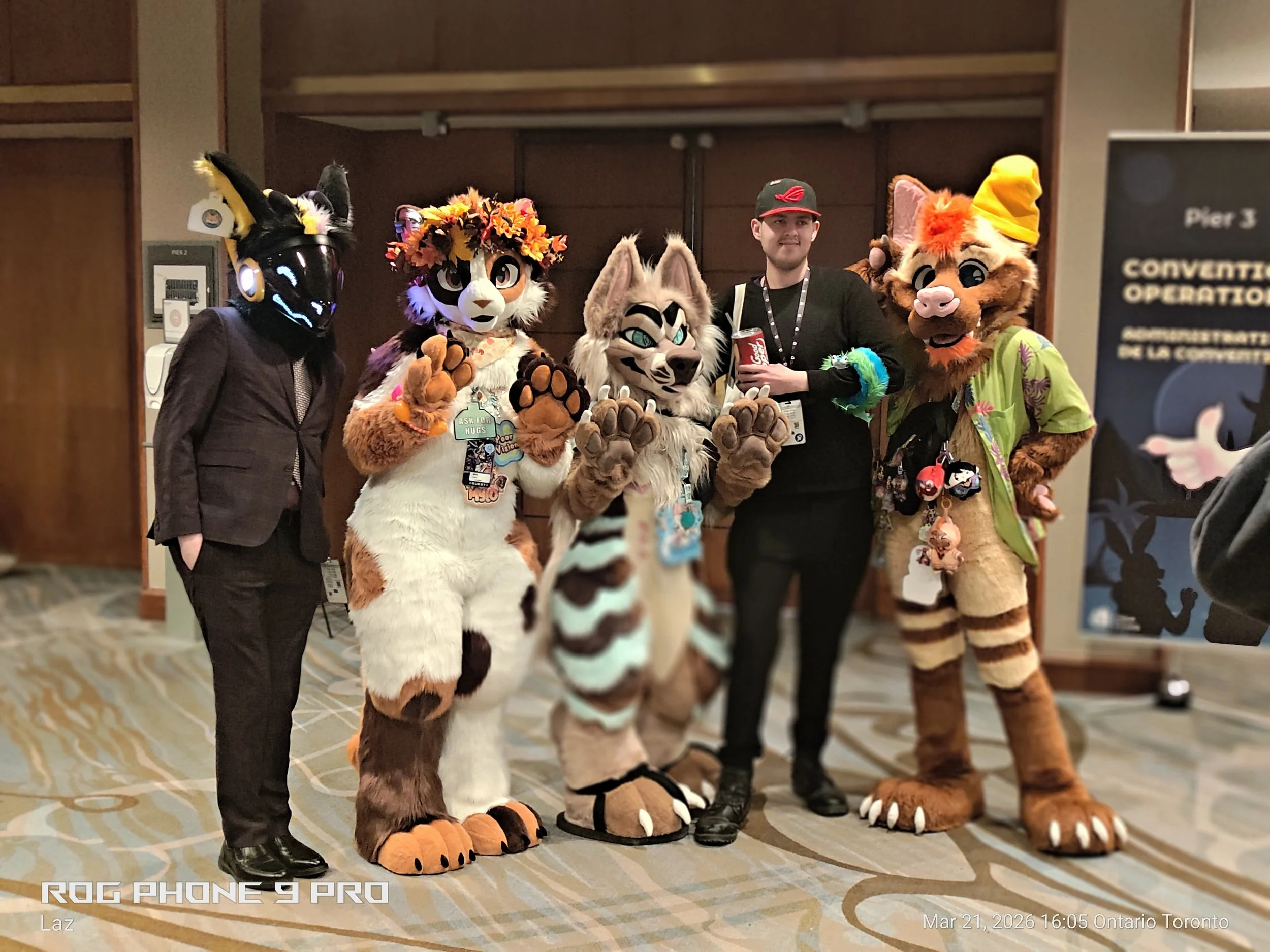 Group of four people dressed in animal costumes and one person in casual clothing posing for a photo at a convention center.