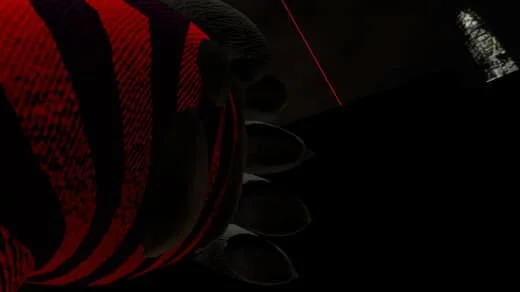 Close-up of a soccer cleat with red and black colors, partially visible on a dark surface.