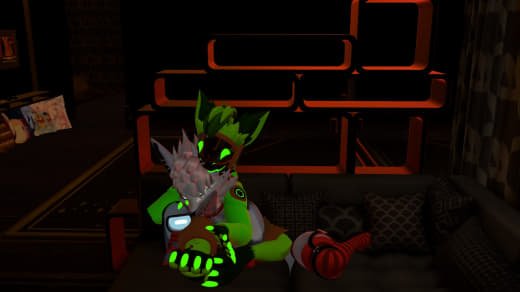 Furry anthropomorphic character with green and black fur, wearing a green shirt and black pants, sitting on a couch with red and black headphones and plush toys, in a room with illuminated orange and black shelving.