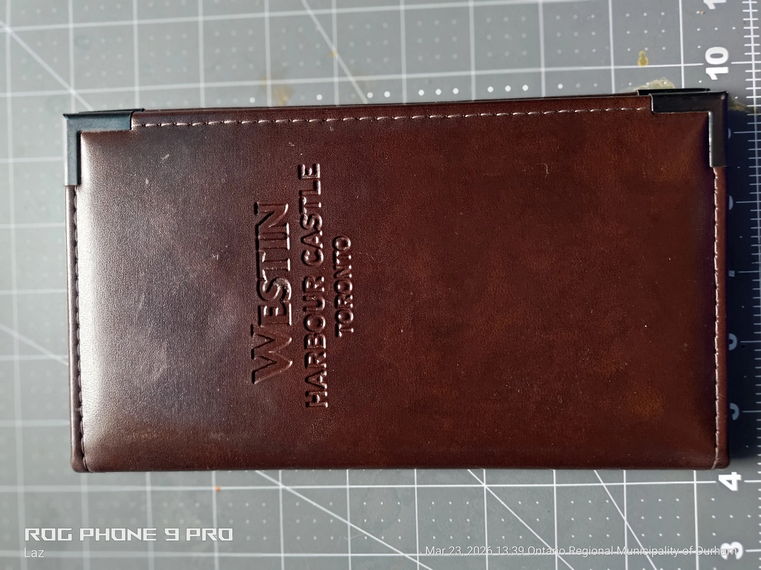 Close-up of a brown leather wallet with embossed text on the surface, placed on a gray cutting mat with measurement markings.