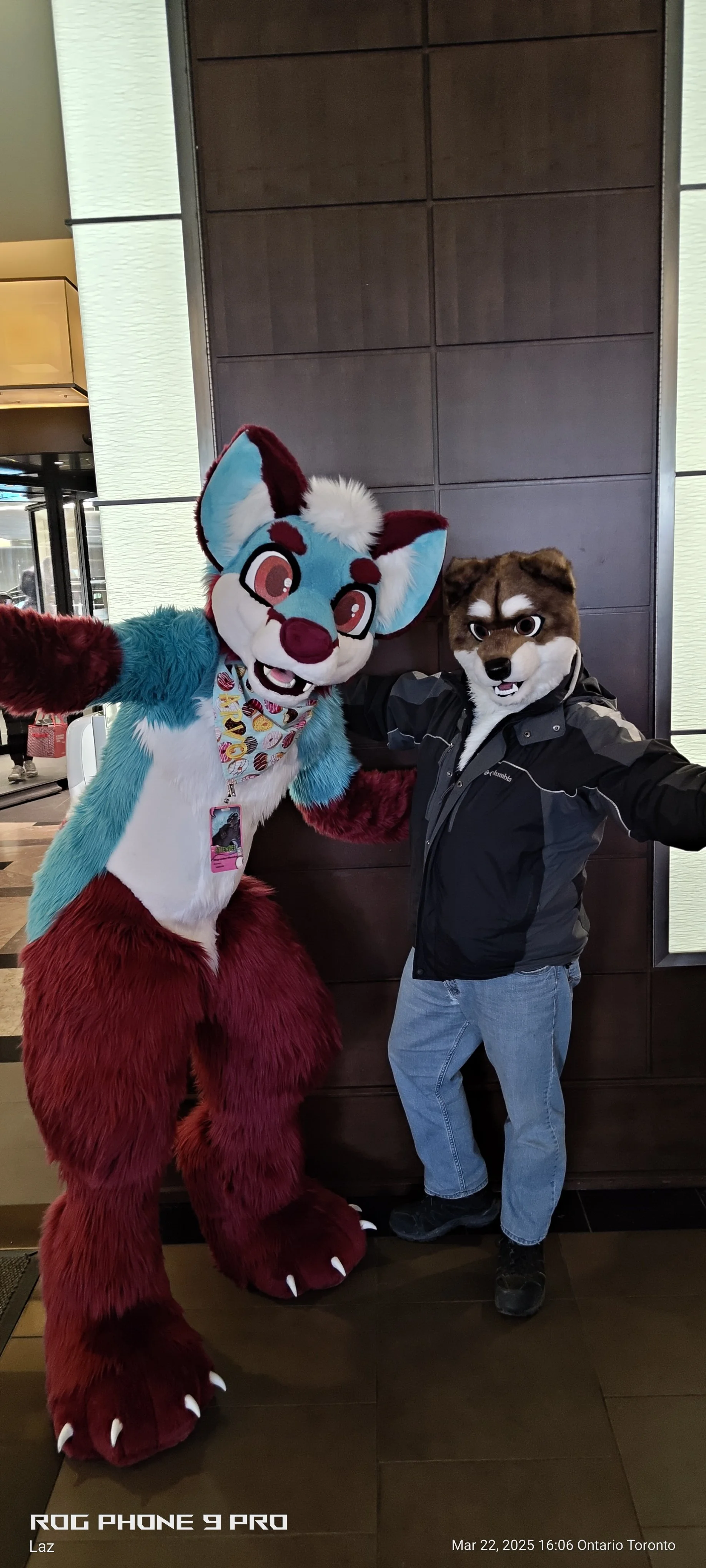 A person wearing a wolf mask and a person in a colorful lion mascot costume taking a selfie together indoors.