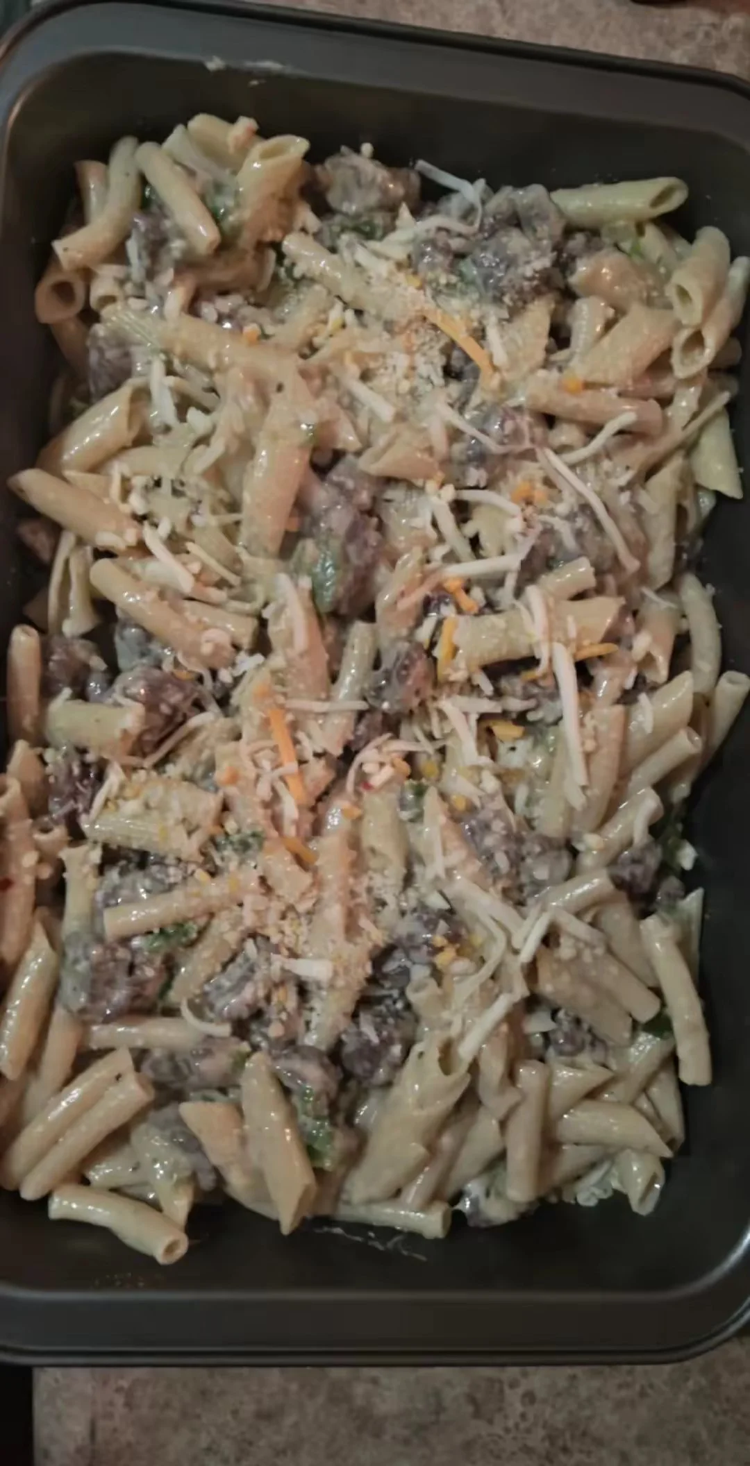 Baked pasta casserole with penne, cooked meat, cheese, and vegetables in a baking dish.