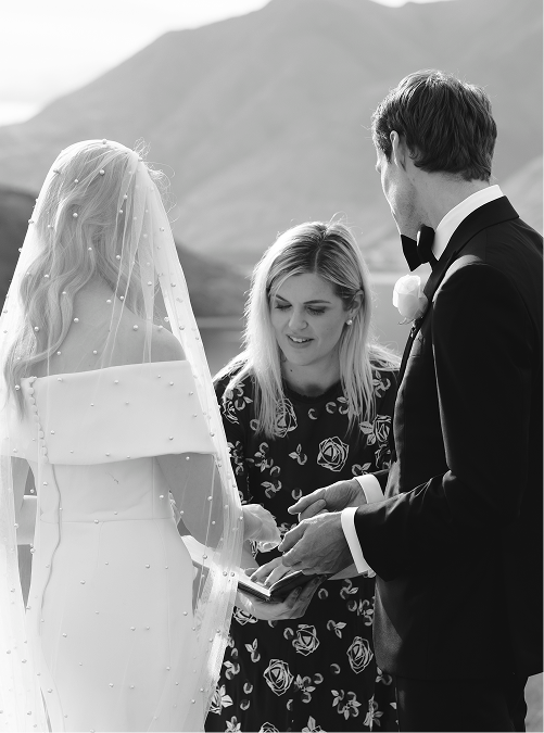 A couple getting married outdoors with an officiant during the ceremony, mountain landscape in the background.