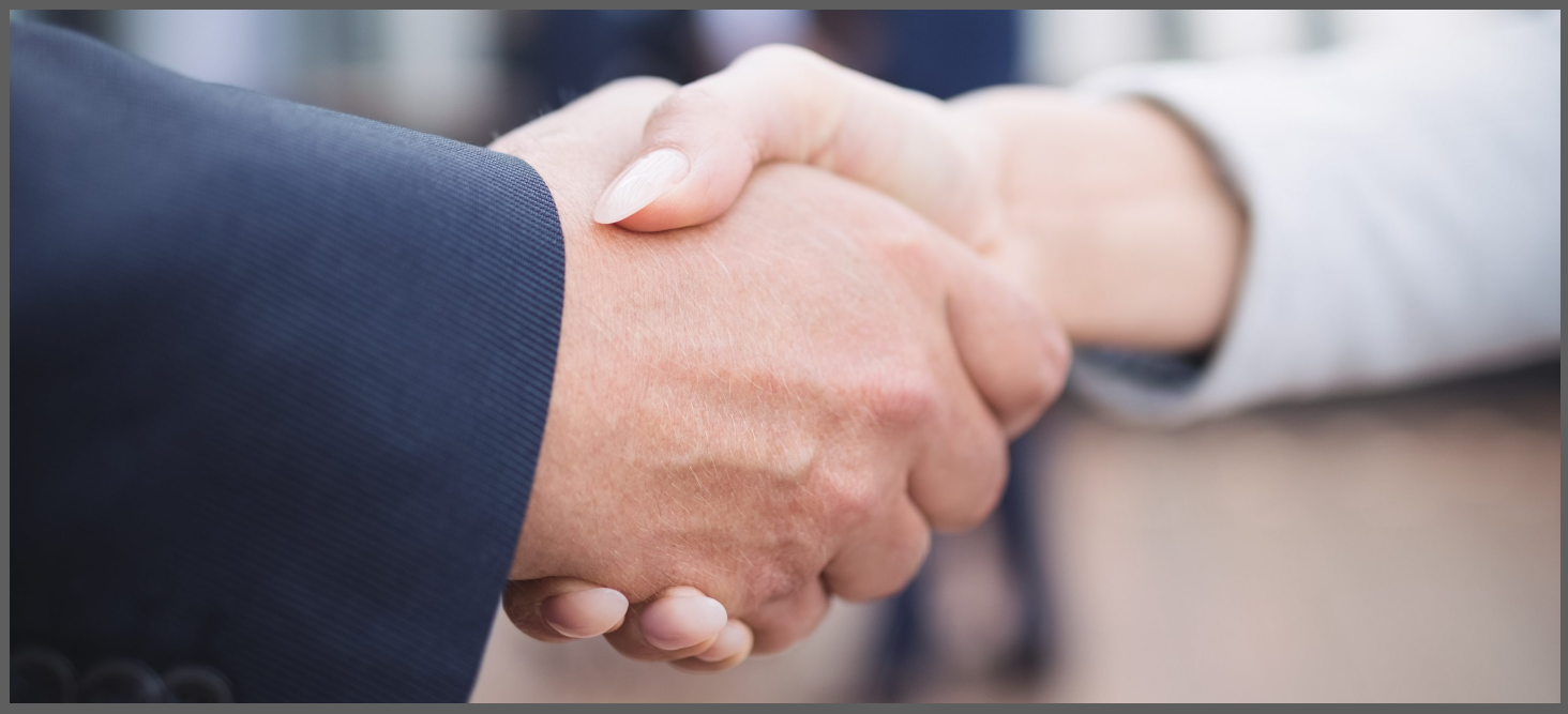 Close-up of a handshake between a man wearing a dark blue jacket, and a woman wearing a light gray jacket.