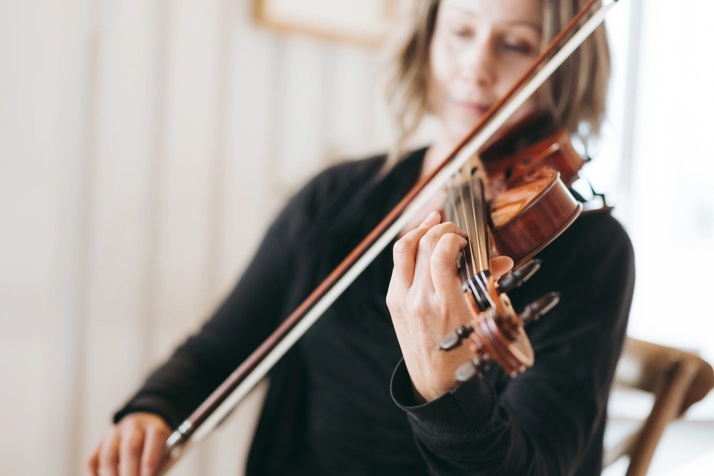 A person playing a violin indoors, focusing on the violin and their hand on the strings.