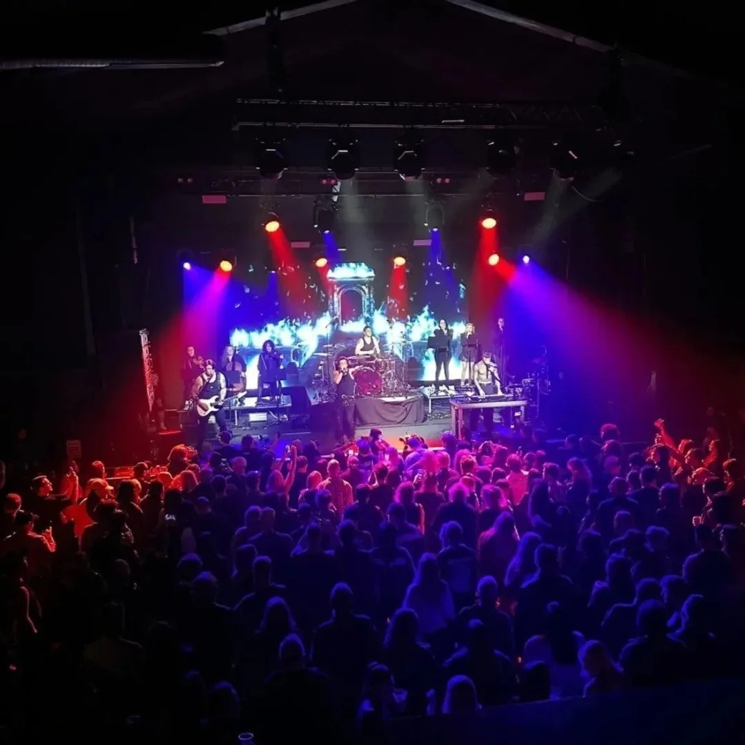 A live concert on stage with colorful lighting and a band performing, audience dancing and enjoying the show.