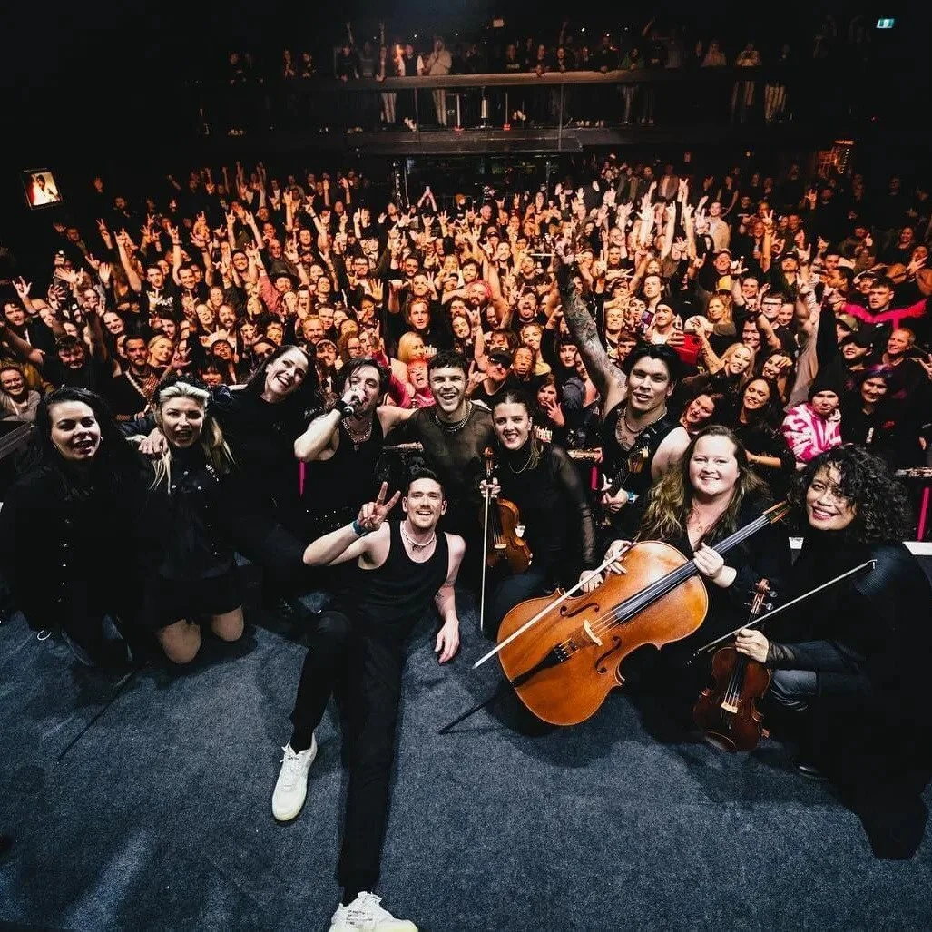 Group of musicians on stage with an audience in the background, celebrating after a performance.