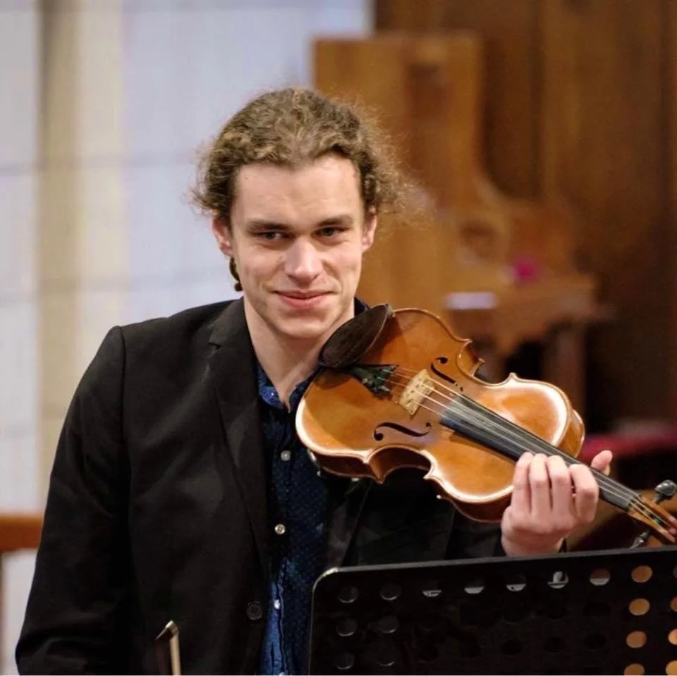 Young man with curly hair playing a violin in a music room.