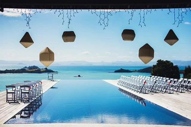 Infinity pool overlooking the ocean with white lounge chairs on either side and hanging lanterns above.