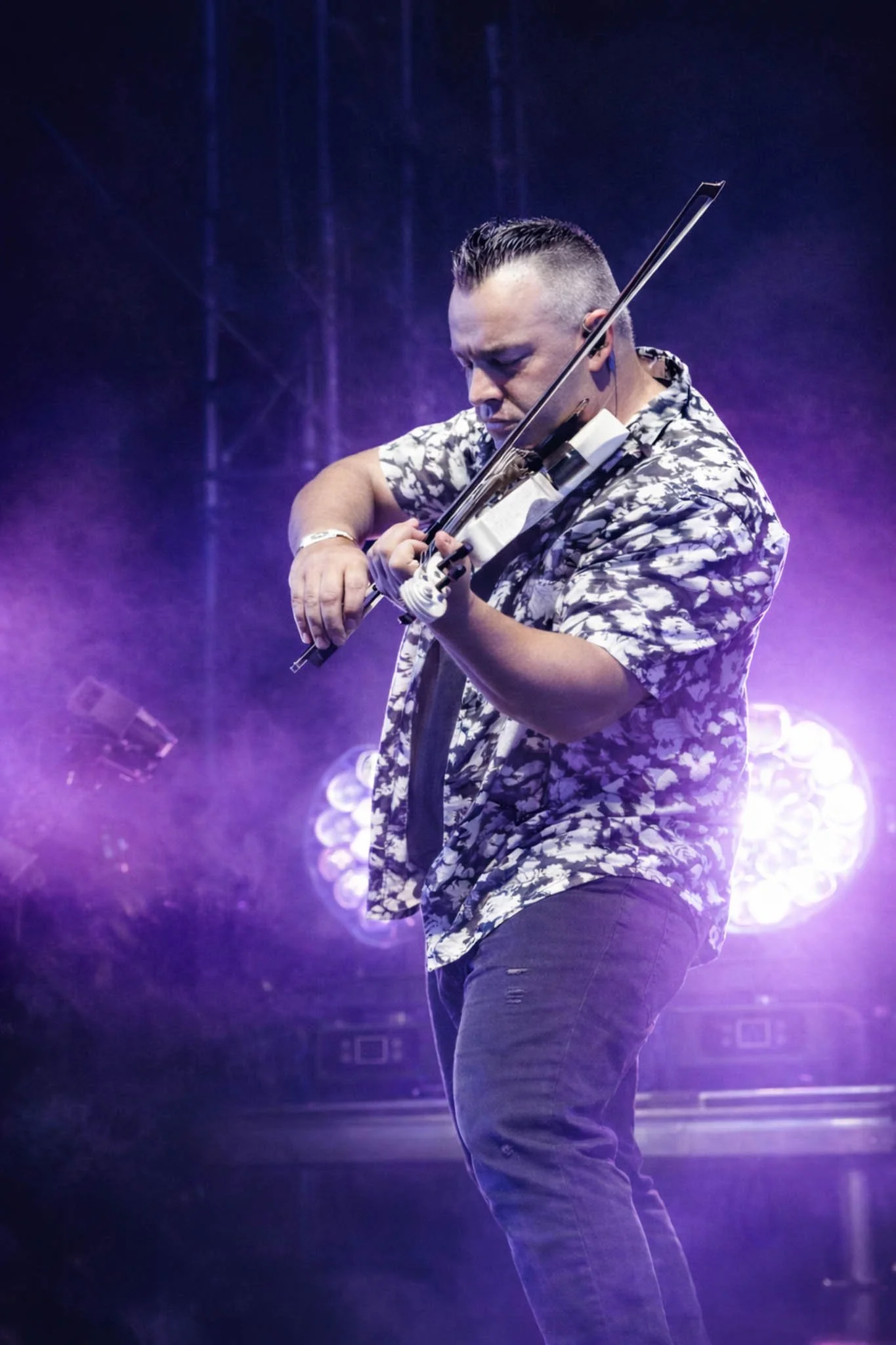 Man playing violin on stage with purple lighting and blurred background.