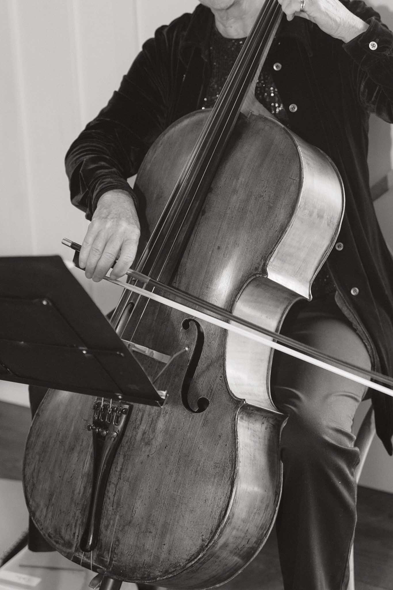 A person playing a cello, holding the bow and pressing the strings with their left hand. The image is in black and white.