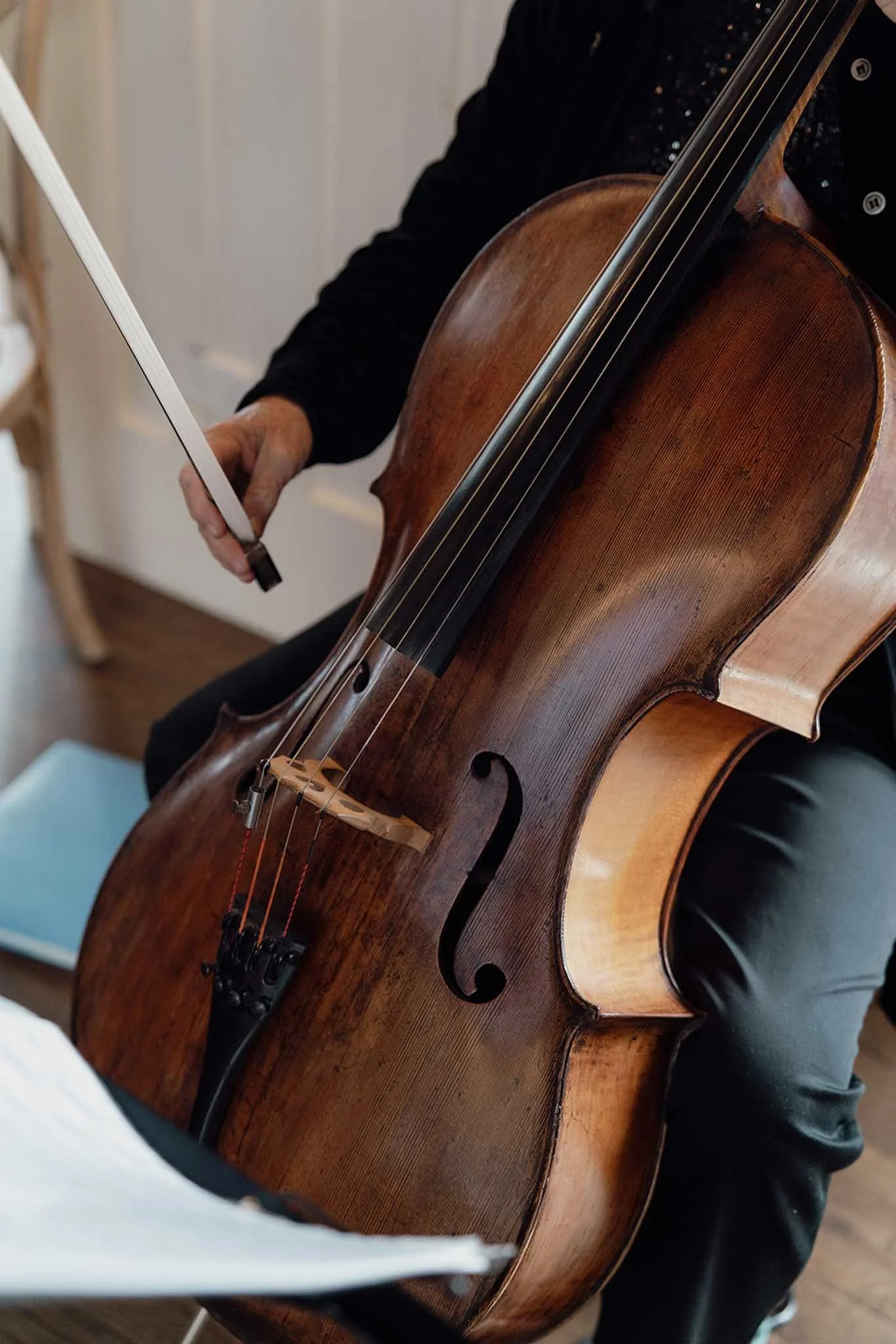Person playing a brown wooden acoustic cello with a black fingerboard and metallic strings