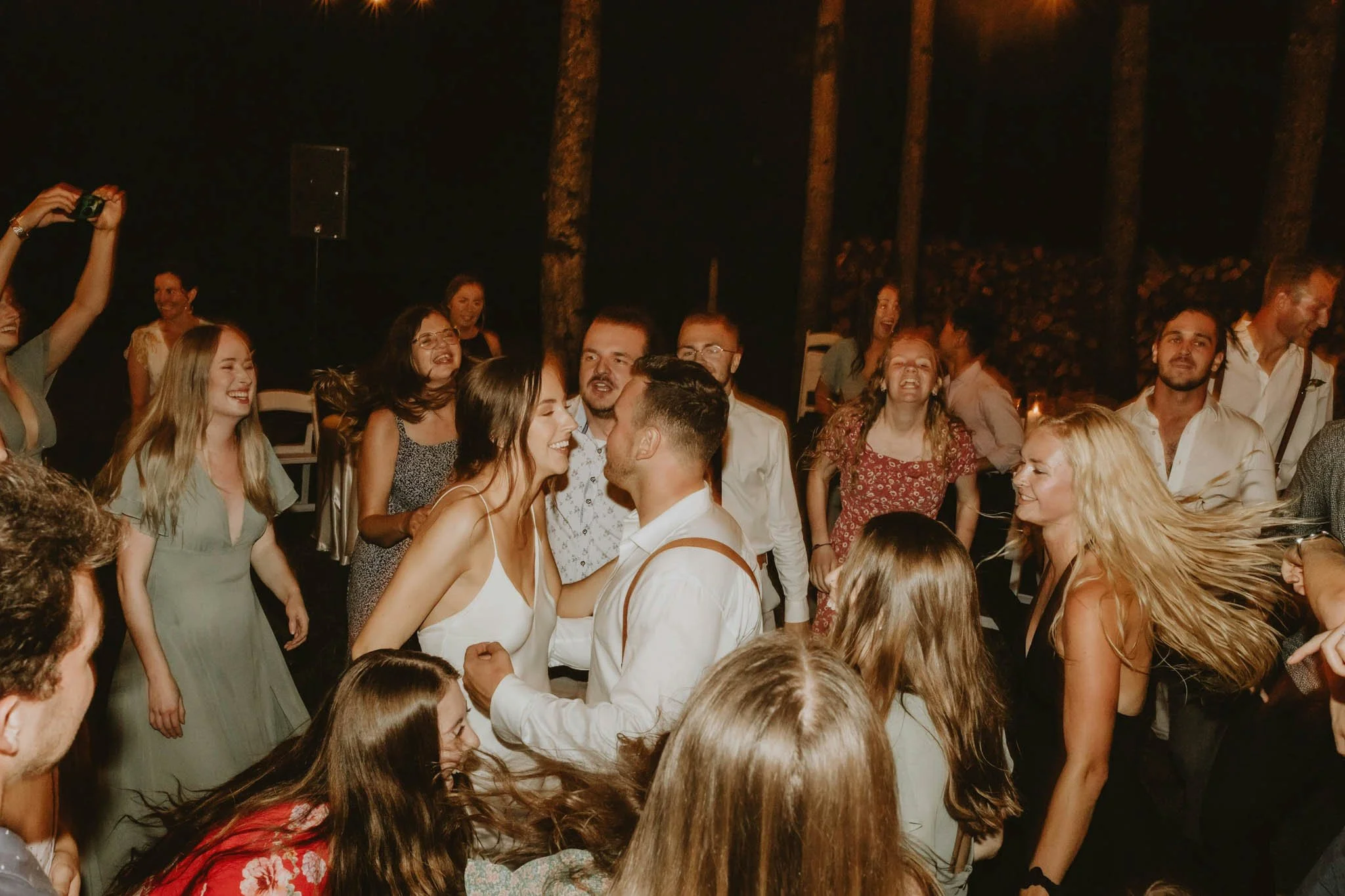 People dancing and celebrating at an outdoor night event, with a man and woman in the center sharing a tender moment.
