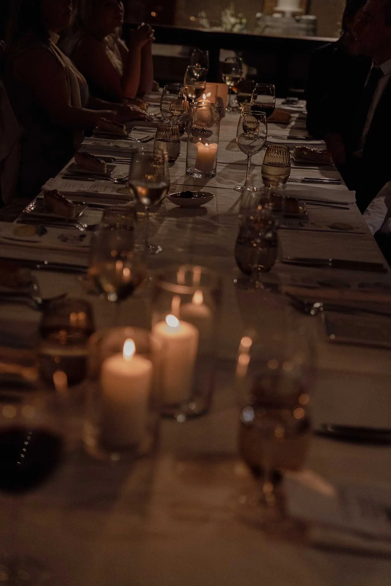 A dimly lit dinner table with candles and glasses of wine, with several people seated around it.